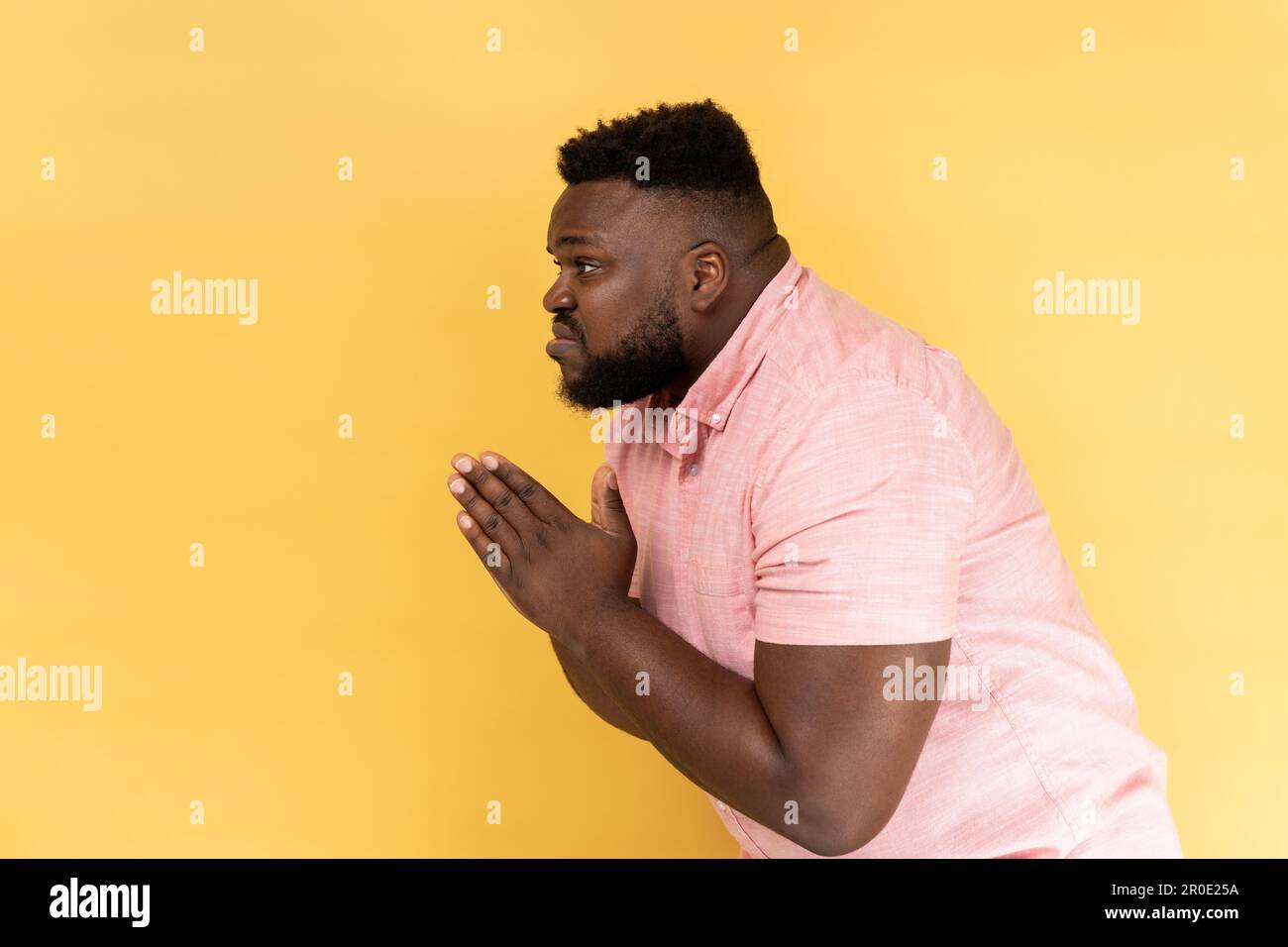 S'il vous plaît, je suis pardonne mendiant. Vue latérale de l'homme inquiet contrarié portant une chemise rose à la recherche de la grimace désespérée implorant, priant pour de l'aide. Studio d'intérieur isolé sur fond jaune. Banque D'Images