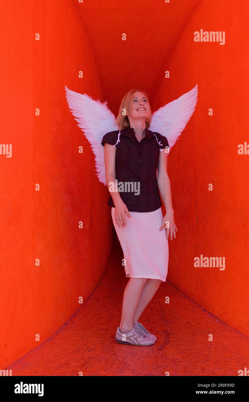 Femme adulte de taille moyenne portant des ailes d'ange dans un tunnel rouge Banque D'Images