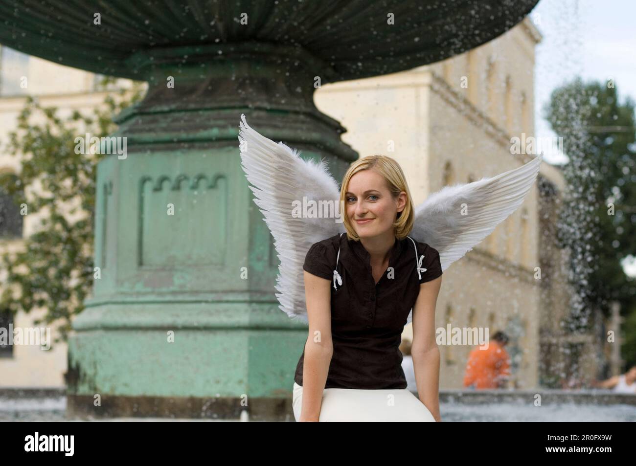 Femme adulte de taille moyenne portant des ailes d'ange assise près d'une fontaine à l'université, Munich, Bavière, Allemagne Banque D'Images