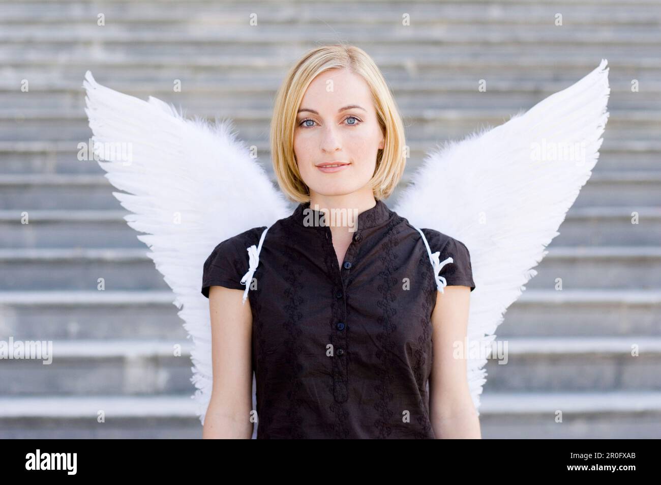 Femme adulte de taille moyenne portant des ailes d'ange devant un escalier Banque D'Images