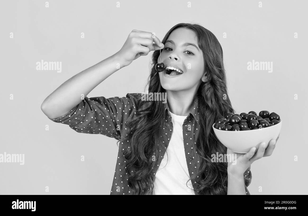 une jeune fille positive mange un bol de cerise sur fond jaune Banque D'Images