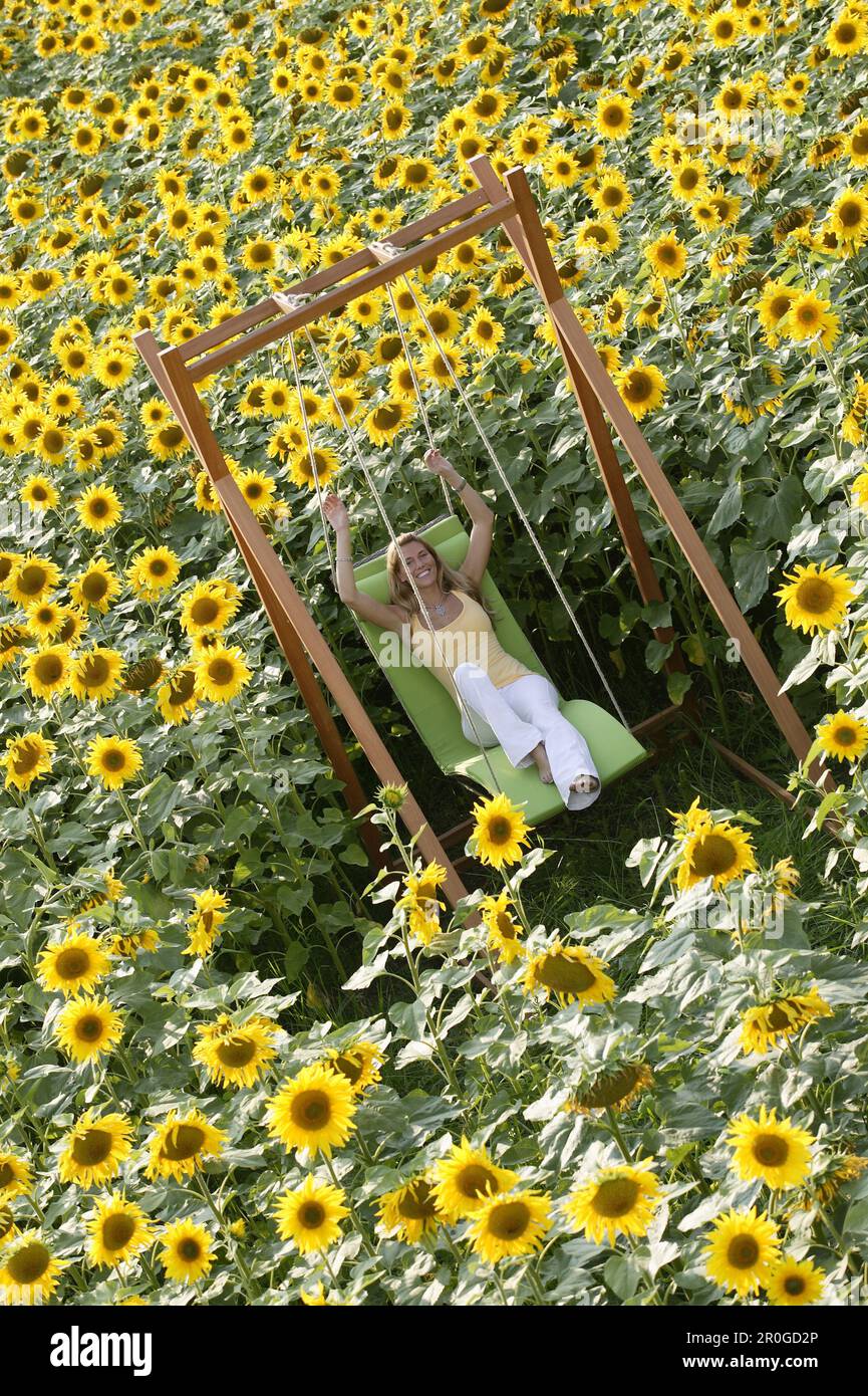 Jeune femme assise sur une balançoire dans un champ plein de tournesols, Bavière, Allemagne Banque D'Images