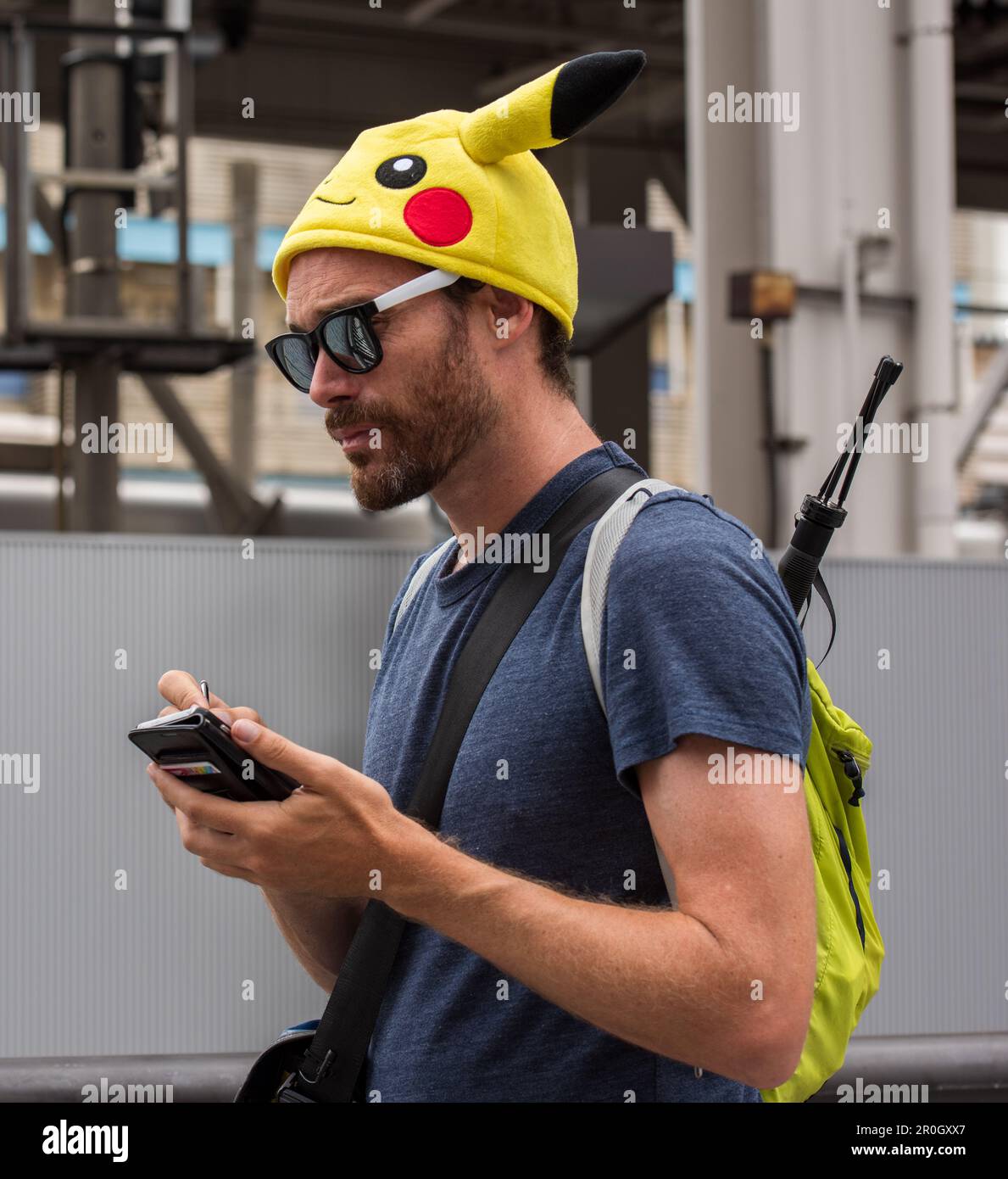 L'homme, portant un chapeau Pikachu et un sac à dos, utilise un stylet pour faire une note sur le smartphone. Banque D'Images