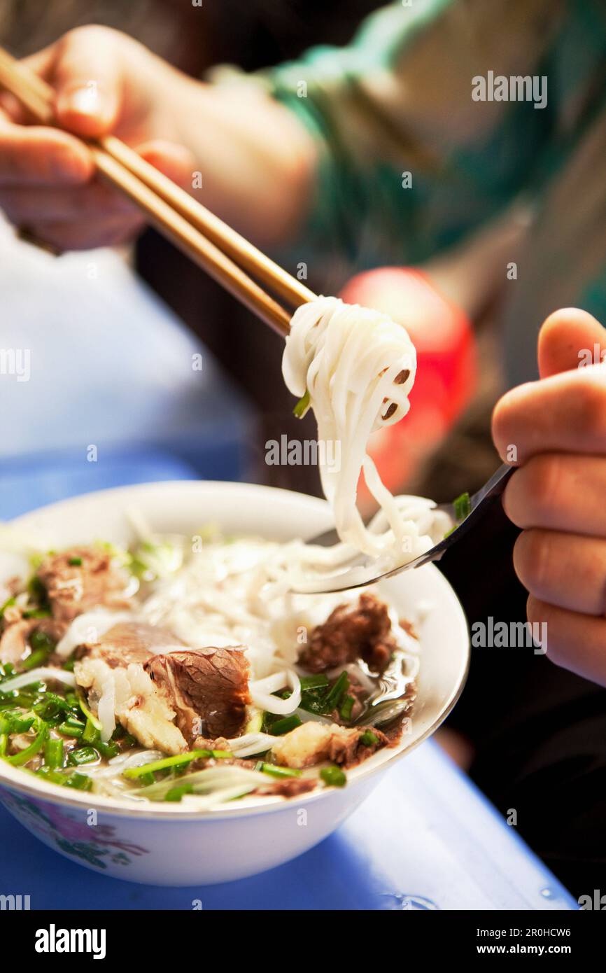 VIETNAM, Hanoi, restaurant Pho Gia Truyen, également connu sous le nom de 49 Bat Dan, une femme mange une bouchée de pho bo (bol de nouilles de boeuf) de la manière traditionnelle avec un sp Banque D'Images