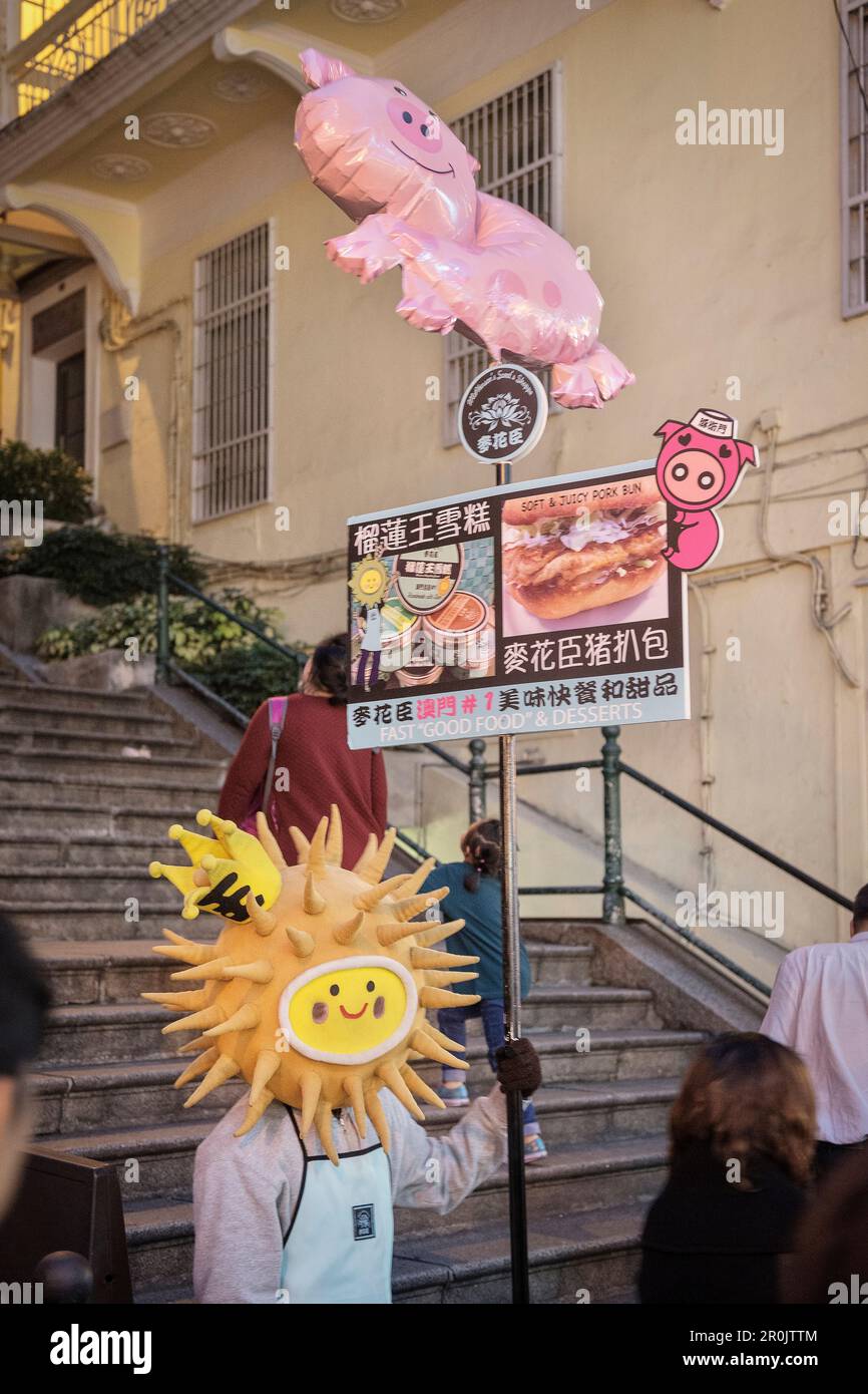 Homme habillé tenant une publicité pour un restaurant dans la vieille ville de Macao, Chine, Asie Banque D'Images