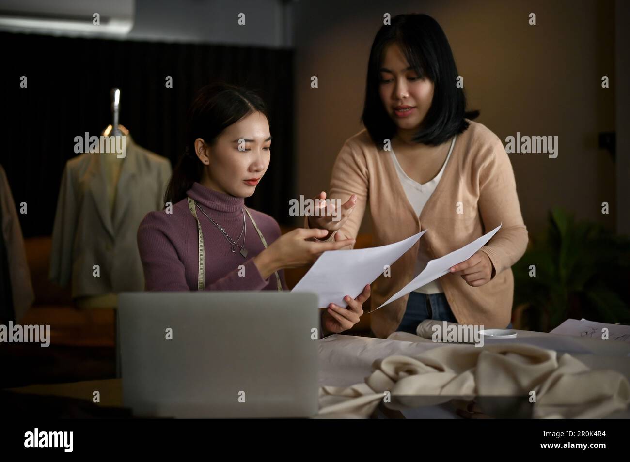 Deux stylistes ou tailleurs de mode asiatiques millénaires professionnels discutent de leur nouvelle collection et travaillent ensemble en studio. Banque D'Images