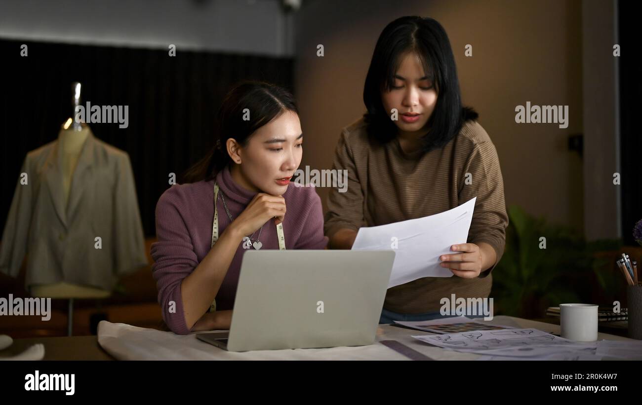 Deux couturières asiatiques ou designers de mode discutent du modèle de leur nouvelle collection et travaillent ensemble en studio. Banque D'Images