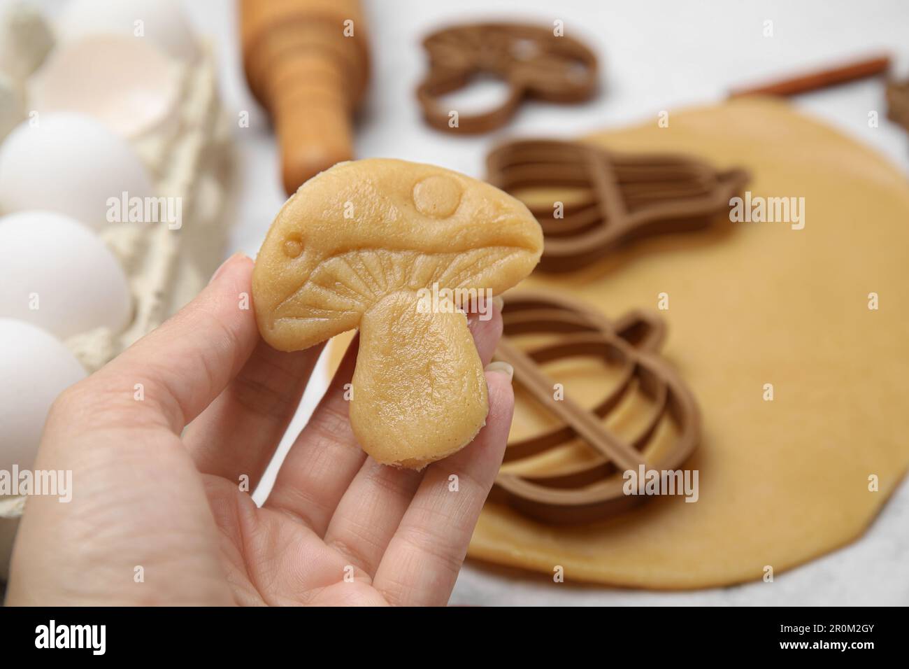 Femme tenant un biscuit en forme de champignon non cuit à la table blanche, gros plan Banque D'Images