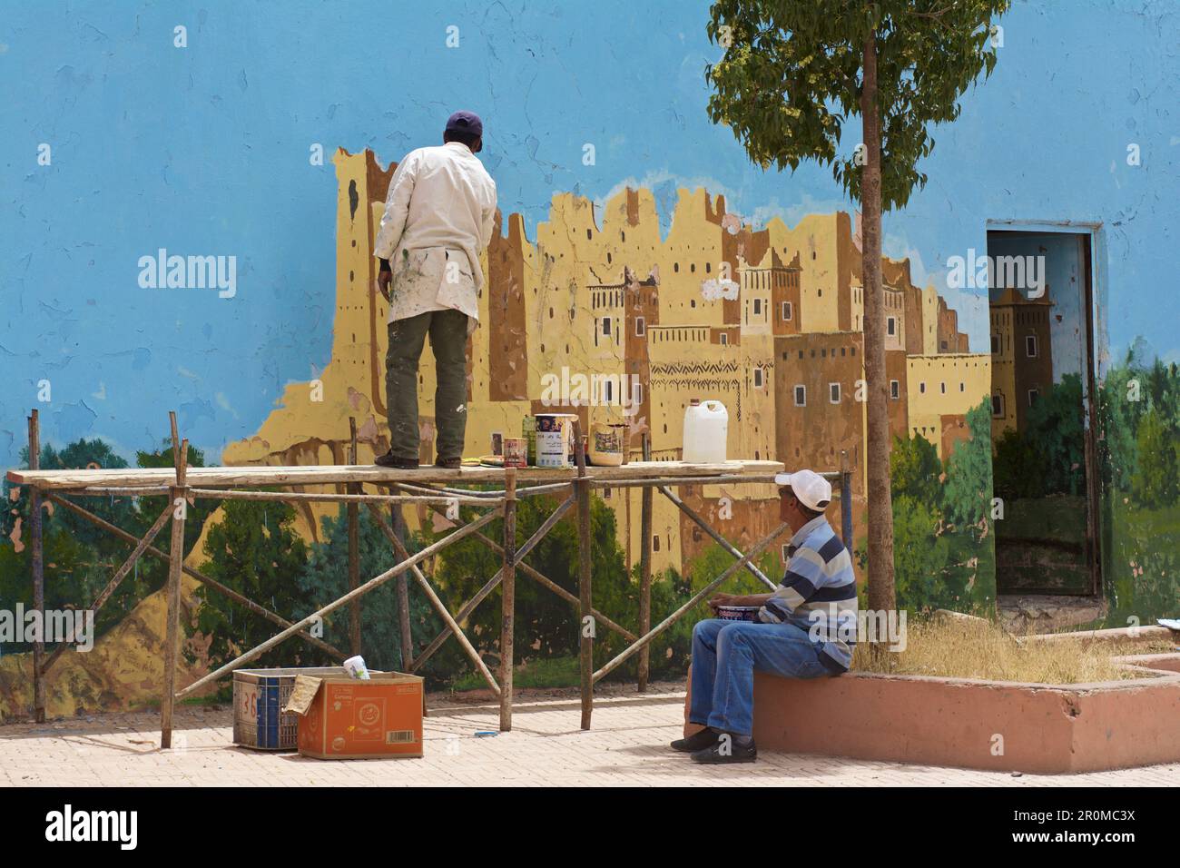 Des hommes peignent un mur à El Kela m'Gouna avec une kashbah, Haut Atlas de Dadestal, Maroc Banque D'Images