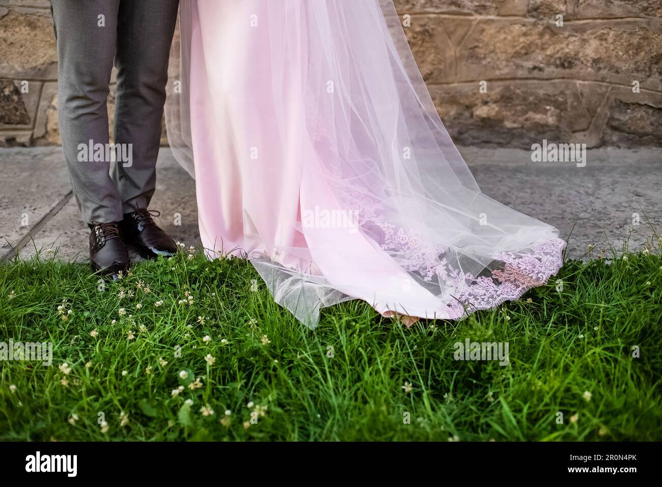 Mariage couple jambes debout ensemble sur pelouse verte. Mariée et marié. Robe de mariage rose Banque D'Images