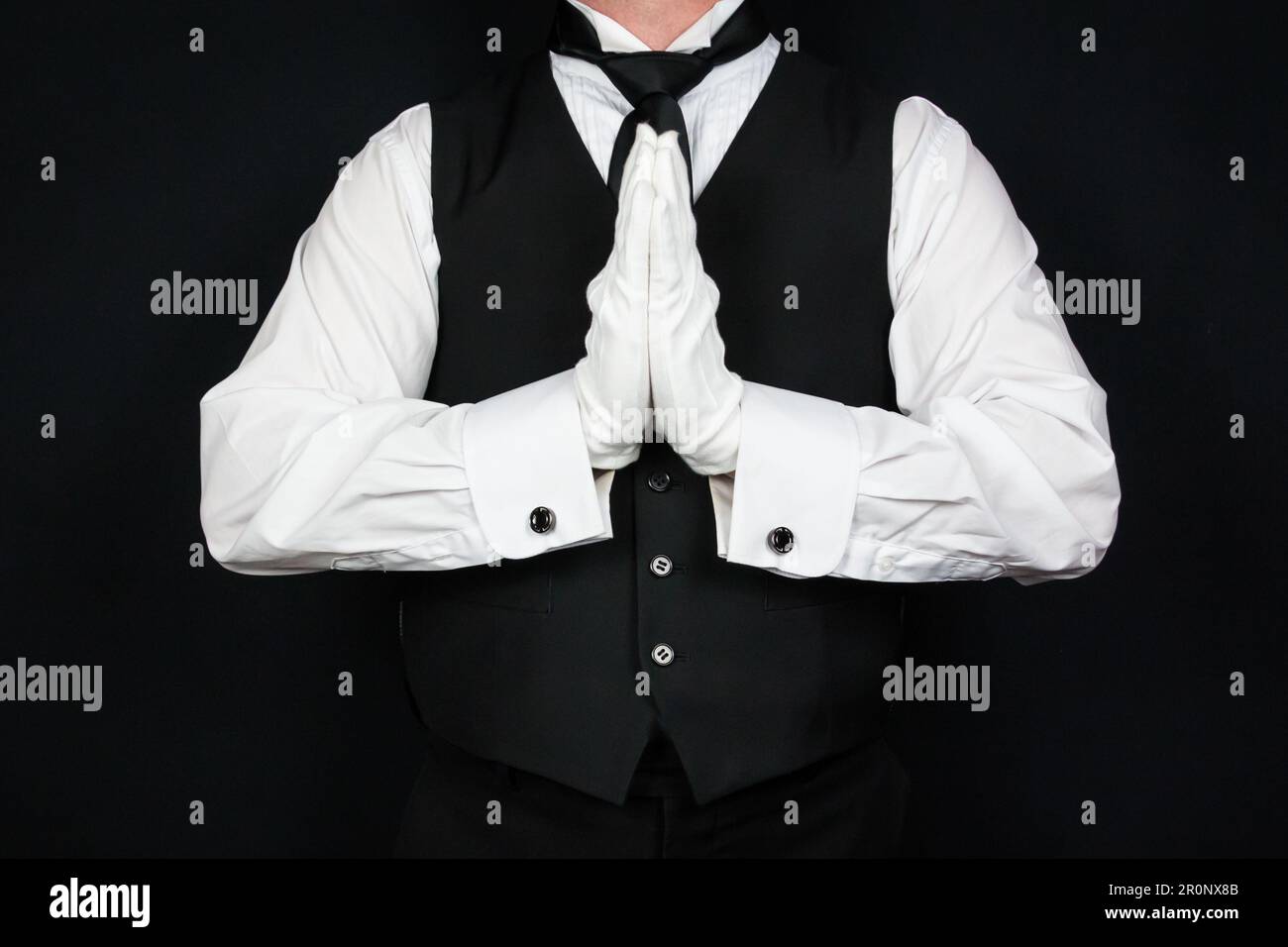Portrait de Butler dans la veste noire et les gants blancs tenant les mains dans la prière. Industrie des services et respect et courtoisie professionnels. Banque D'Images