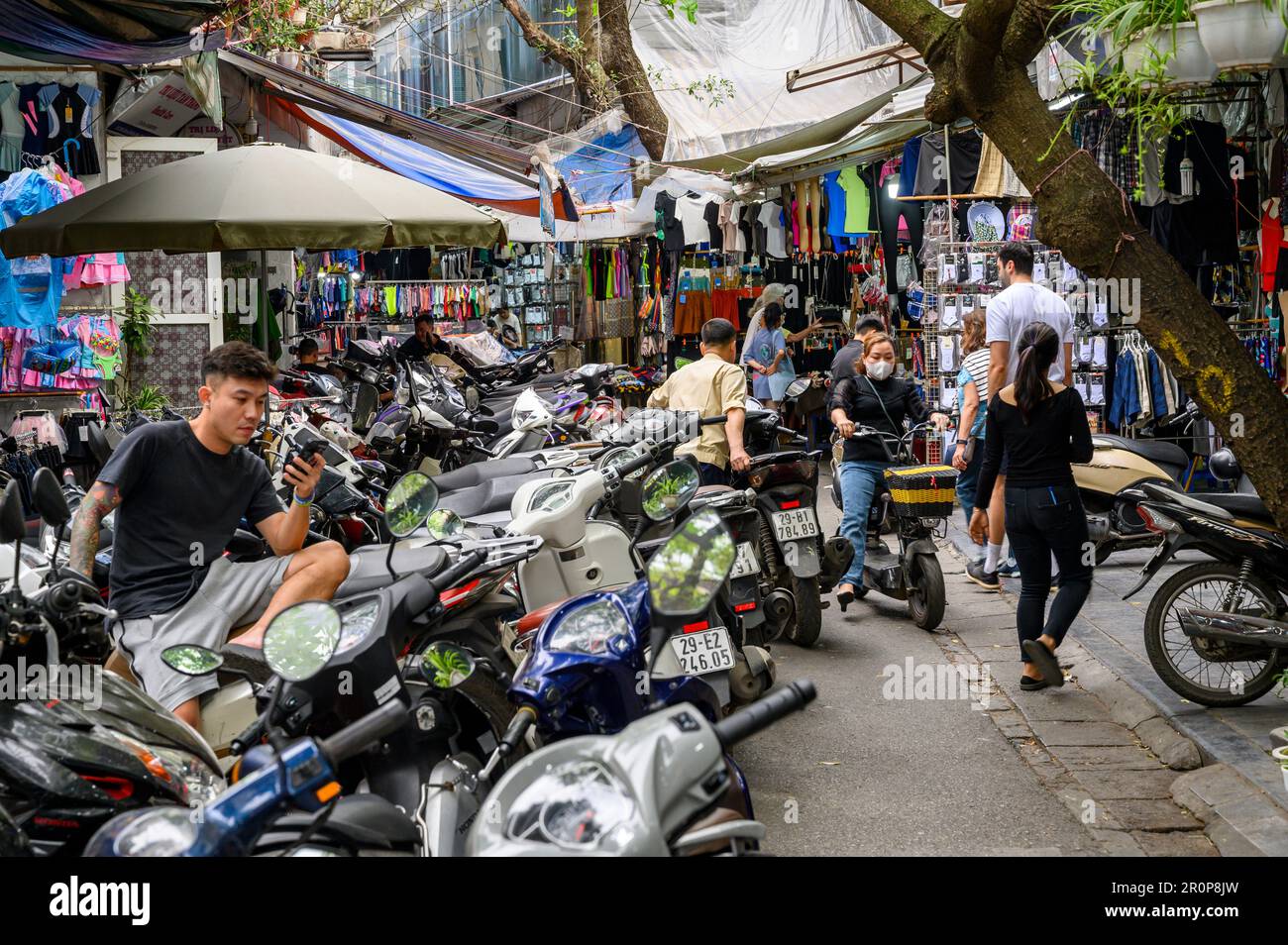 Rue étroite dans le vieux quartier remplie de cyclomoteurs garés et de petits magasins indépendants à Hanoi, Vietnam. Banque D'Images