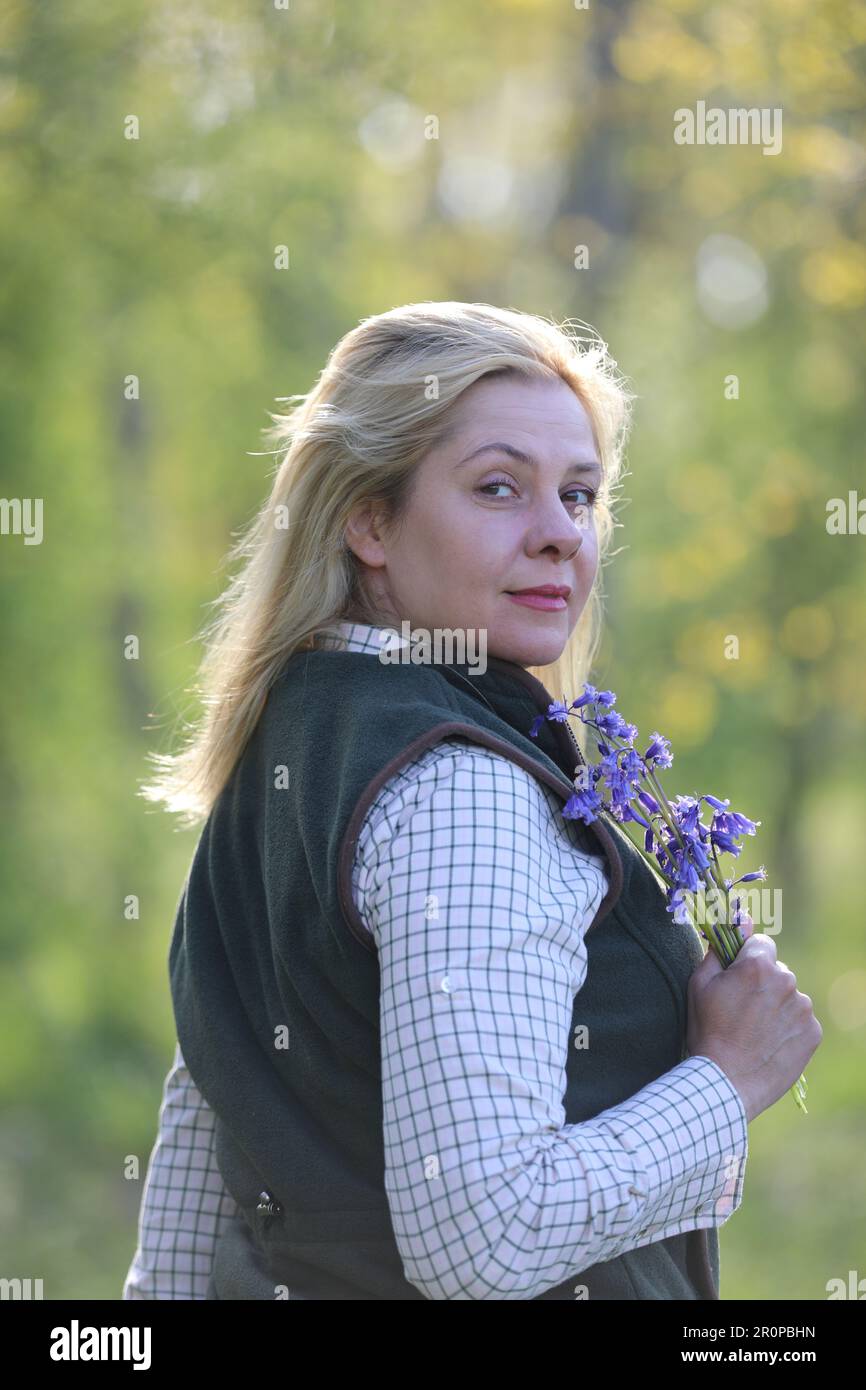 Une femme debout dans un bois de bluebell tenant un groupe de bluebells Banque D'Images