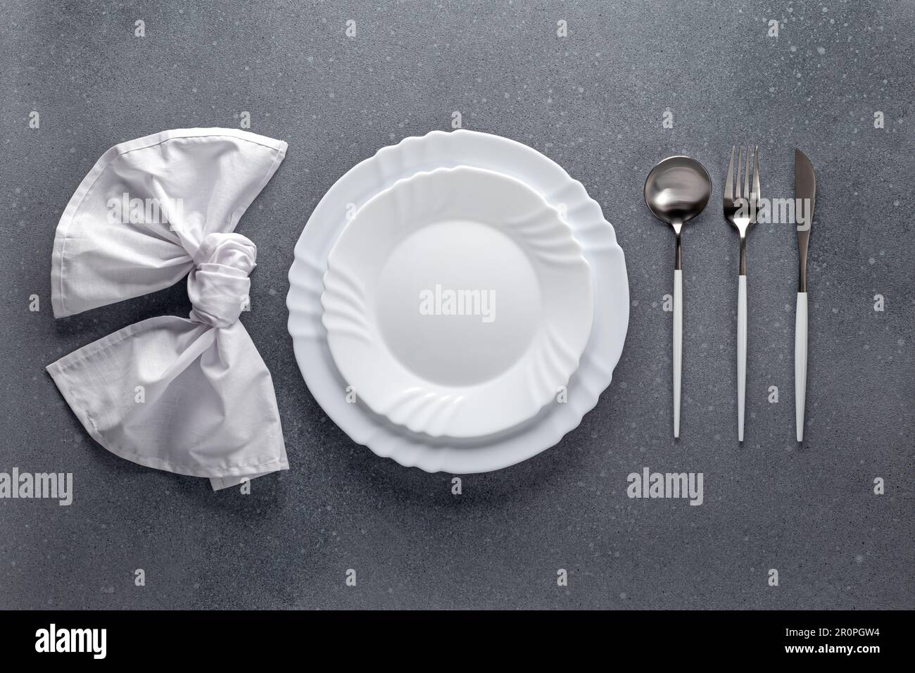 Placez le cadre avec une serviette blanche, une assiette vide et des couverts argentés sur une table à gravoir en béton gris. Vue de dessus. Dîner de fête dans un café. Modèle de menu, fl Banque D'Images