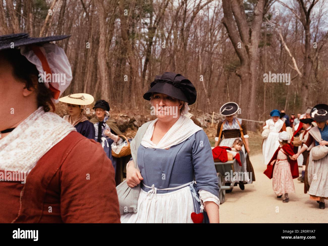 Lexington, Massachusetts États-Unis - avril 2023 - les femmes et les enfants dans la période coloniale robe marcher avec tous leurs effets le long de la route de combat dans la minute Banque D'Images