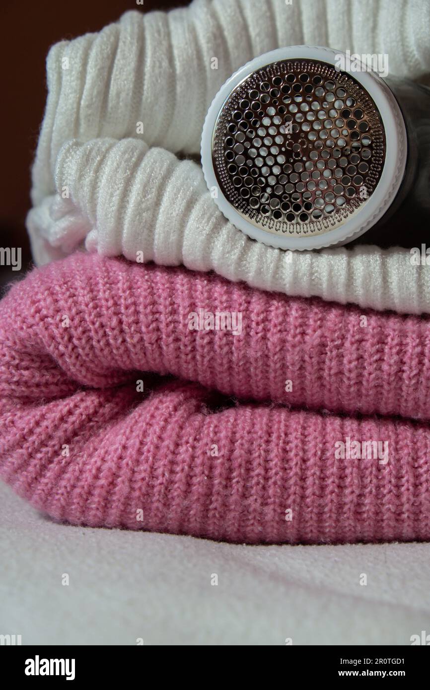Rasoir anti-pilling. Appareil pour le rasage des vêtements. Rasoir en tissu anti-peluche. Chandail électrique portable en pillule defuzzer décharneur de peluches de l'acrylique rose ou de la laine. Rasoir pour appareil électrique après nettoyage et collecte des peluches. Pull en gros plan à piliers. Vieux vêtements d'occasion avec remplissage. Banque D'Images