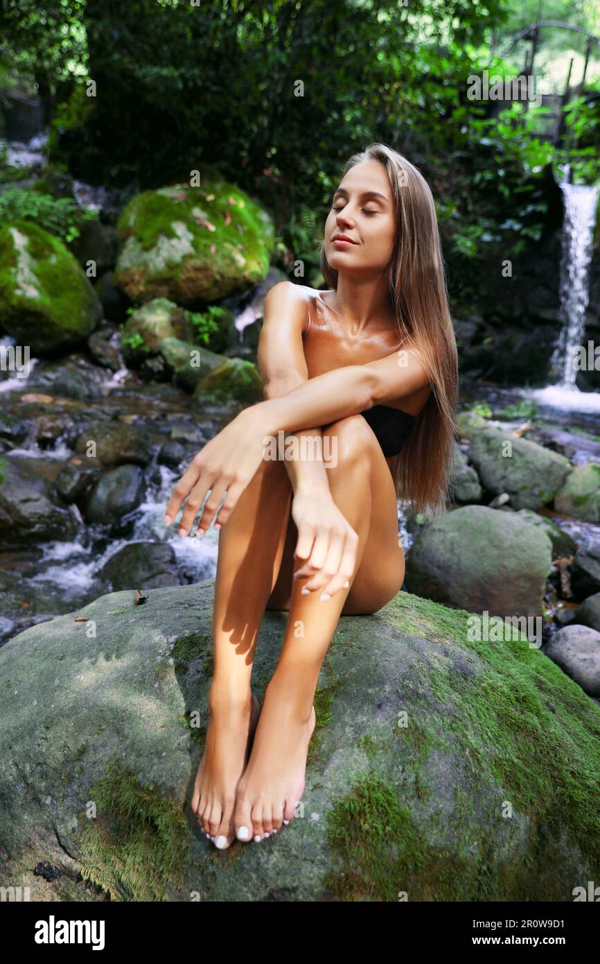 Belle jeune femme en bikini élégant se relaxant près de la cascade de montagne en plein air Banque D'Images