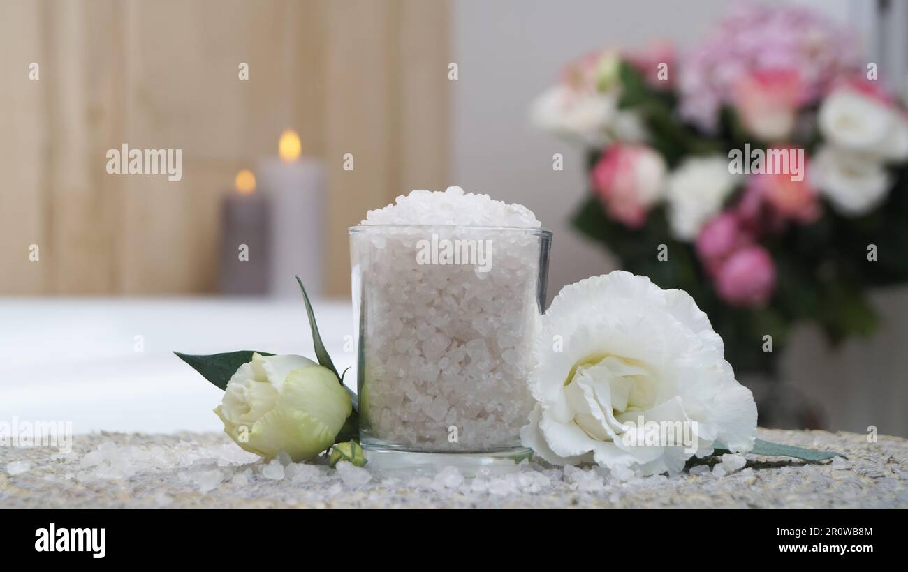 Verre avec sel de bain et belles fleurs sur tapis en osier dans la salle de bains Banque D'Images