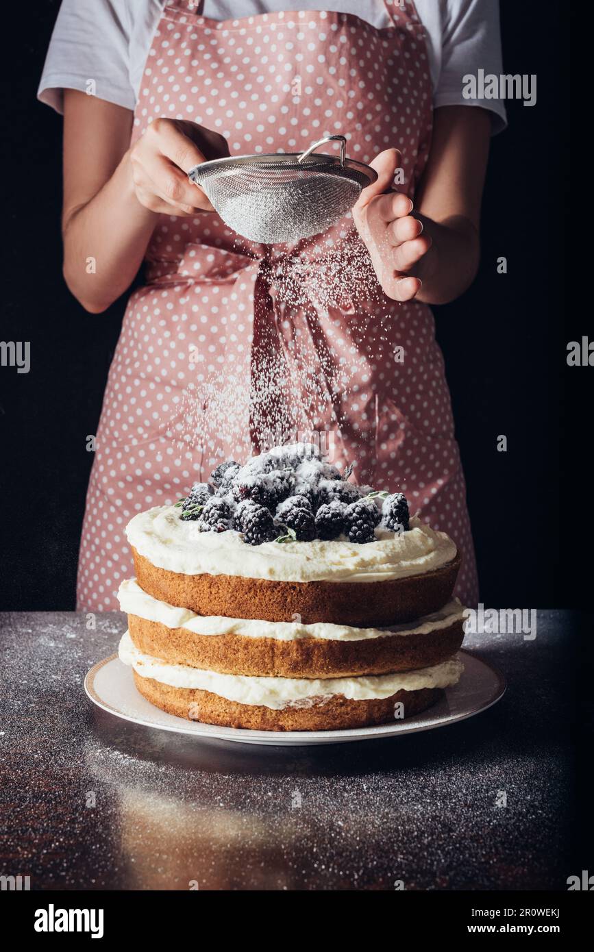 Femme qui a versé de la poudre de sucre sur un BlackBerry savoureux sur du noir Banque D'Images