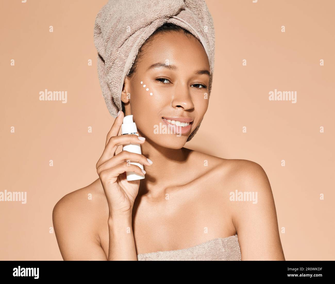 Crème hydratante pour le visage. Belle femme africaine tenant la crème hydratante à la main près de son visage, sur fond pastel. Crème hydratante pour le visage Banque D'Images