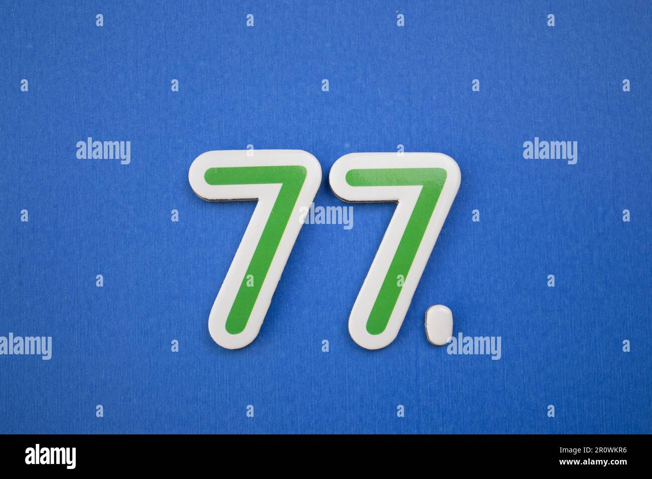 Le numéro 77 de couleur verte, photographié par le dessus, est placé sur un fond bleu. Banque D'Images