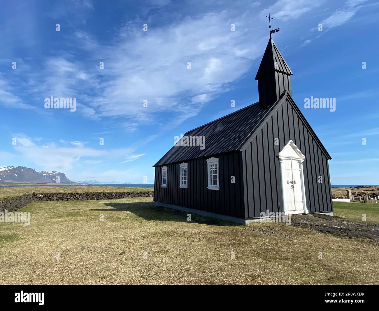 Un bâtiment traditionnel d'église noire avec un clocher et des accents blancs, situé dans un vaste champ herbacé avec un ciel bleu vif au-dessus Banque D'Images