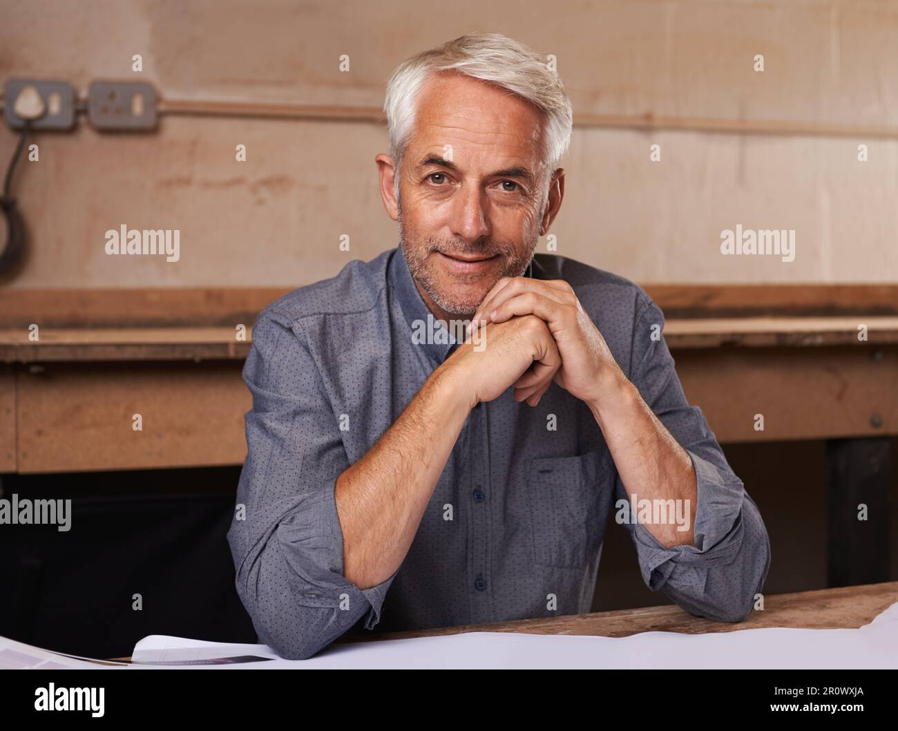 Fier de son atelier. Portrait d'un homme senior assis à son bureau dans son atelier. Banque D'Images