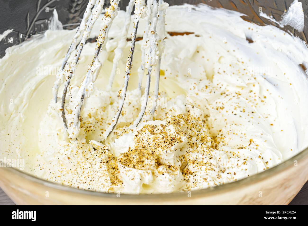 Le fouet mélange une généreuse trempette de fromage de chèvre à la crème avec des noix moulées et du poivre dans un bol en verre, une concentration sélectionnée, une profondeur de champ étroite Banque D'Images