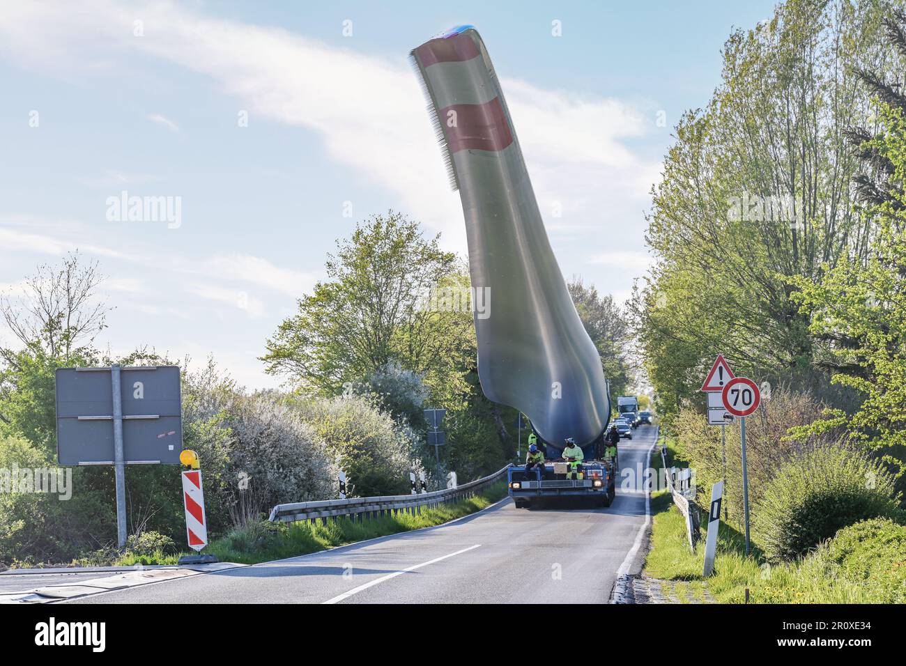 Transport lourd d'une pale d'éolienne levé pour éviter les obstacles et ralentir la circulation sur une route de campagne étroite, industrie pour l'énergie renouvelable, Banque D'Images