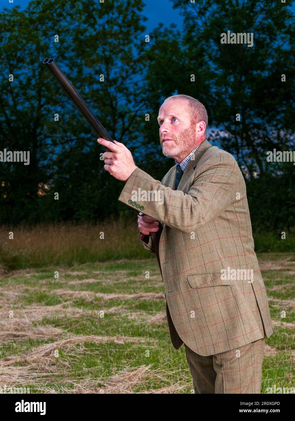 Un homme anglais se tenait au crépuscule dans un costume de tir en tweed avec un fusil de chasse Banque D'Images
