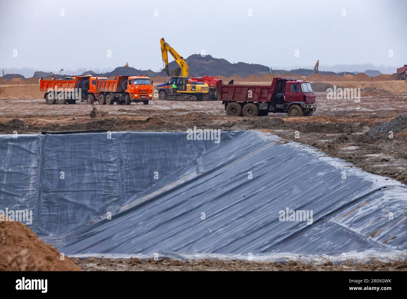Ust-Luga, oblast de Leningrad, Russie - 16 novembre 2021: Construction de fossé de déchets chimiques. Couvercle en plastique de la fosse. Pelles hydrauliques sur le bord. Banque D'Images