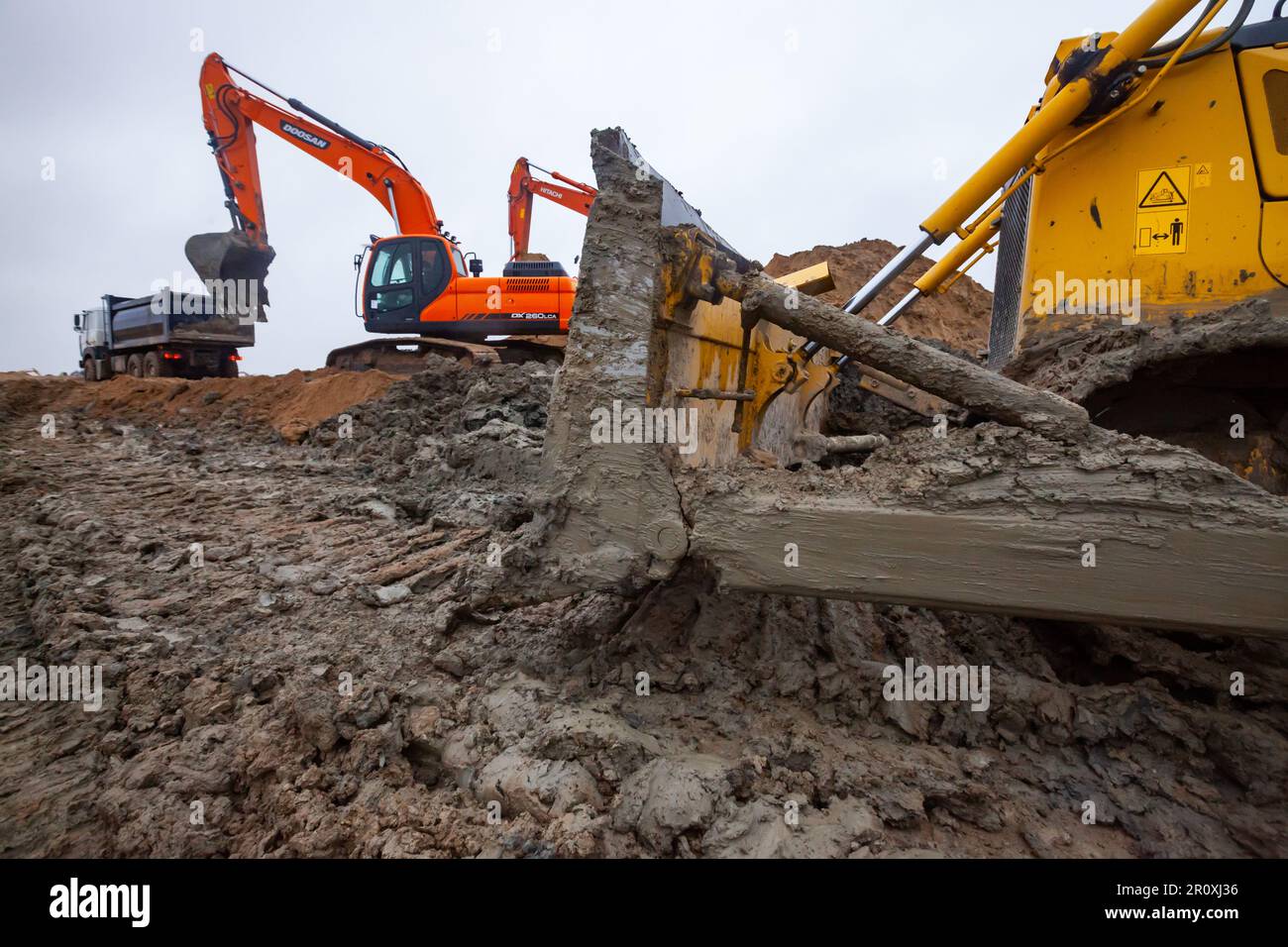 UST-Luga, oblast de Leningrad, Russie - 16 novembre 2021 : excavateurs Doosan et Hitachi sur le chantier. Lame de bouteur dans la boue droite. Jour de pluie, Banque D'Images