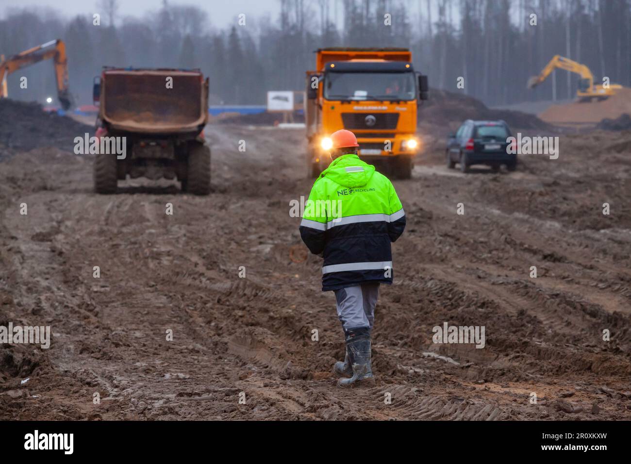 Ust-Luga, oblast de Leningrad, Russie - 16 novembre 2021: Le travailleur va sur la route sale. Machines de construction lourdes en arrière-plan, floues. Banque D'Images