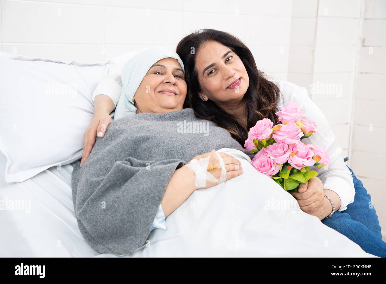 La fille indienne rend visite à sa mère âgée, patiente atteinte d'un cancer, en cours de chimiothérapie à l'hôpital. Femme donner des fleurs à la femme âgée à la clinique. il Banque D'Images