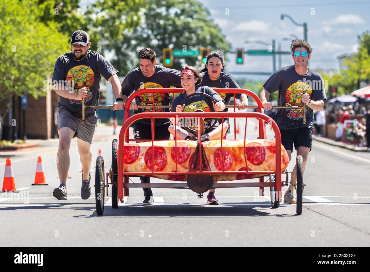 Lawrenceville, GA / Etats-Unis - 22 avril 2023: Une équipe de jeunes adultes pousse un lit dans une rue de ville dans le cadre de la campagne de collecte de fonds Family Promise Bed Race. Banque D'Images