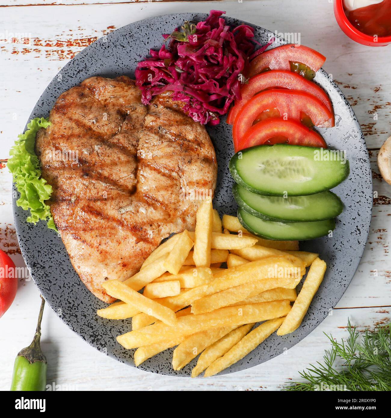 Un délicieux repas avec un steak juteux, des frites croustillantes et une variété de légumes colorés disposés sur une assiette placée sur une table en bois Banque D'Images