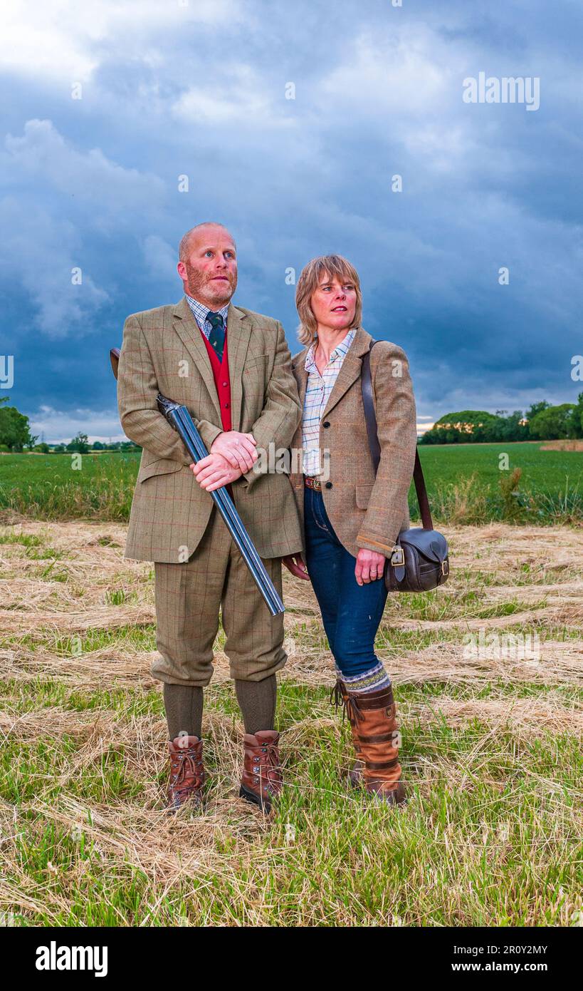 Une dame et un monsieur anglais se tenait au crépuscule dans des combinaisons de tir avec un fusil de chasse Banque D'Images