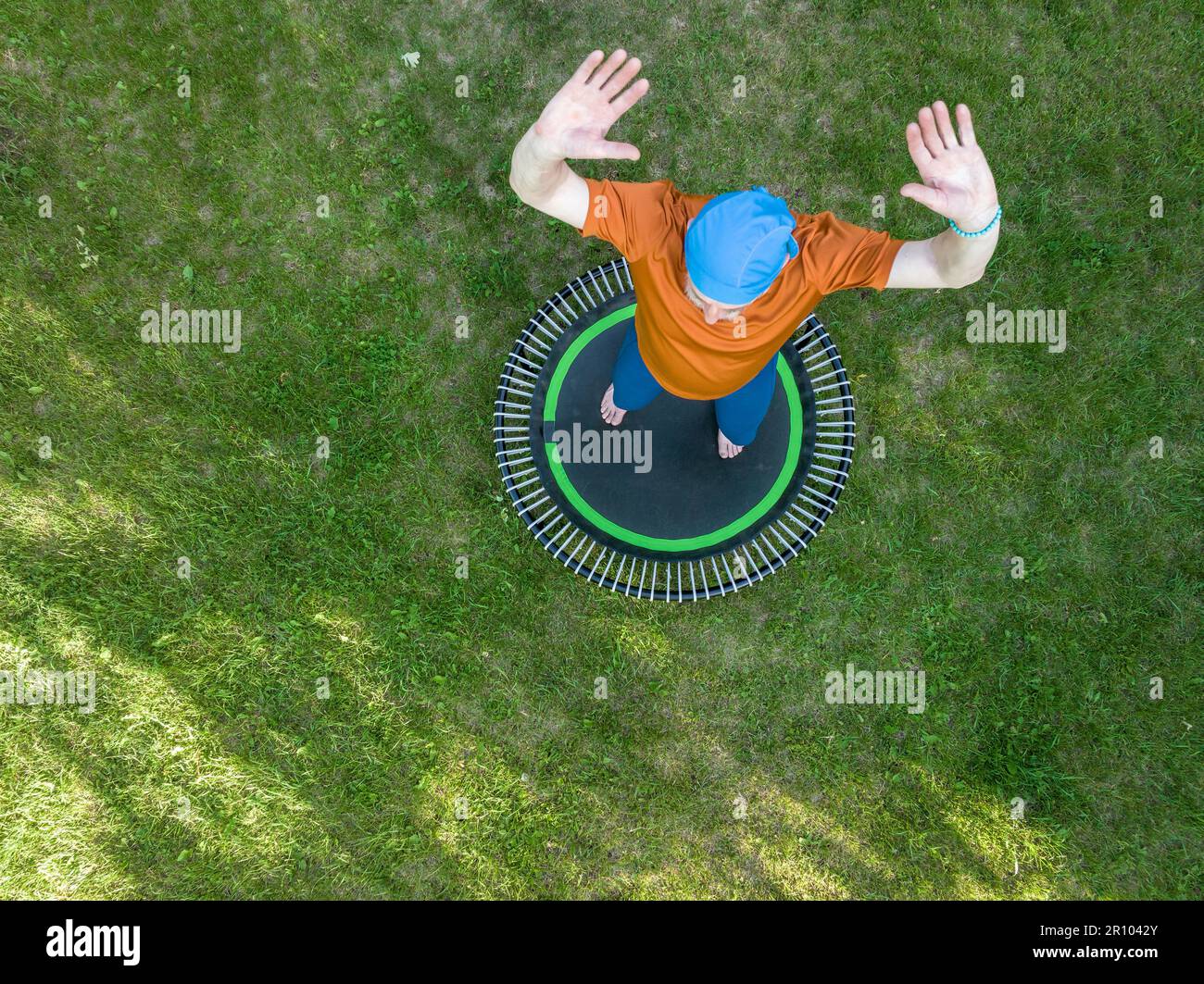 senior surpoids homme s'exerçant sur un mini trampoline dans son arrière-cour, fitness et rebondissement concept, vue aérienne Banque D'Images