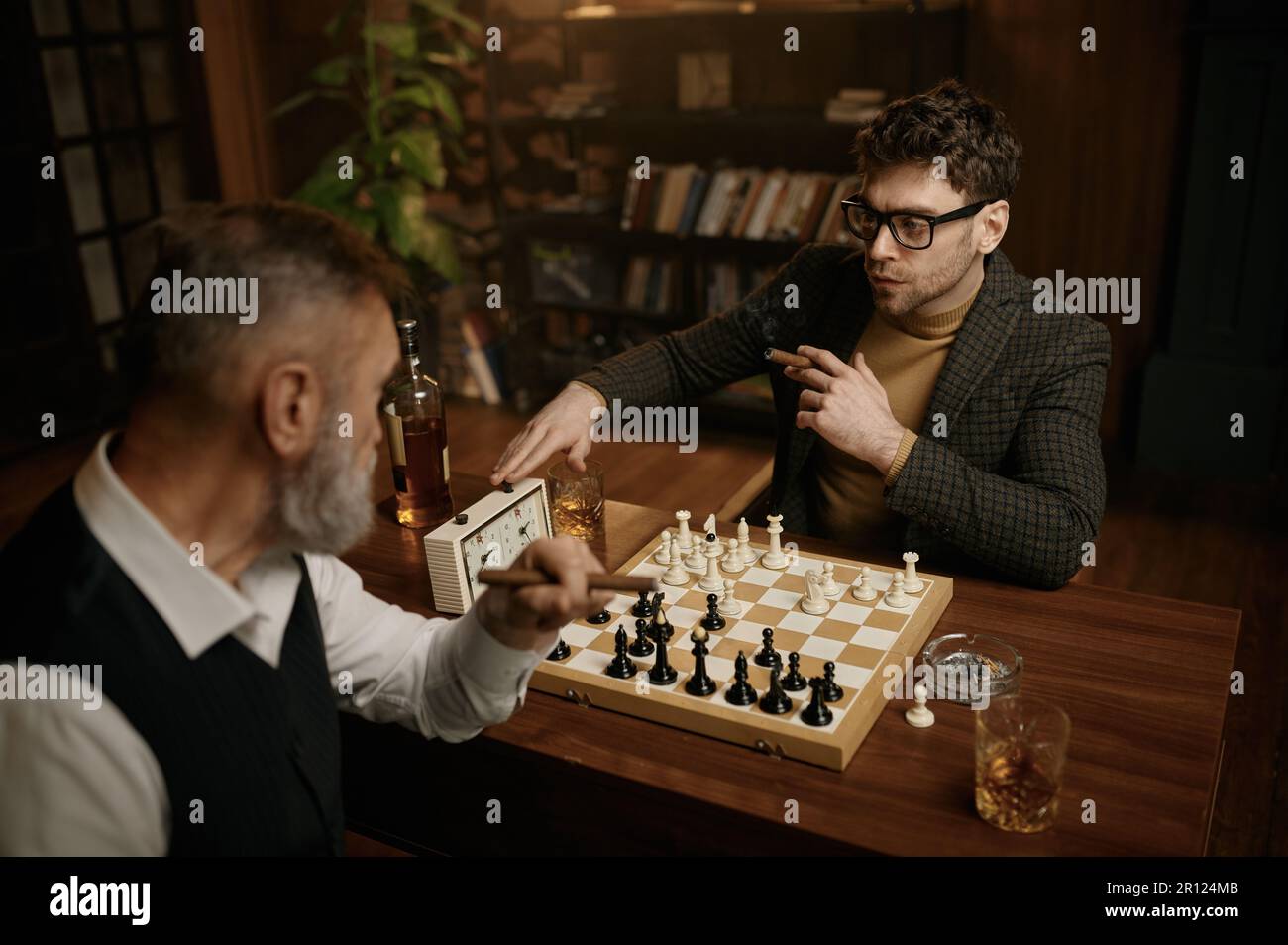 Deux hommes jouant aux échecs assis à table dans le salon de la maison Banque D'Images
