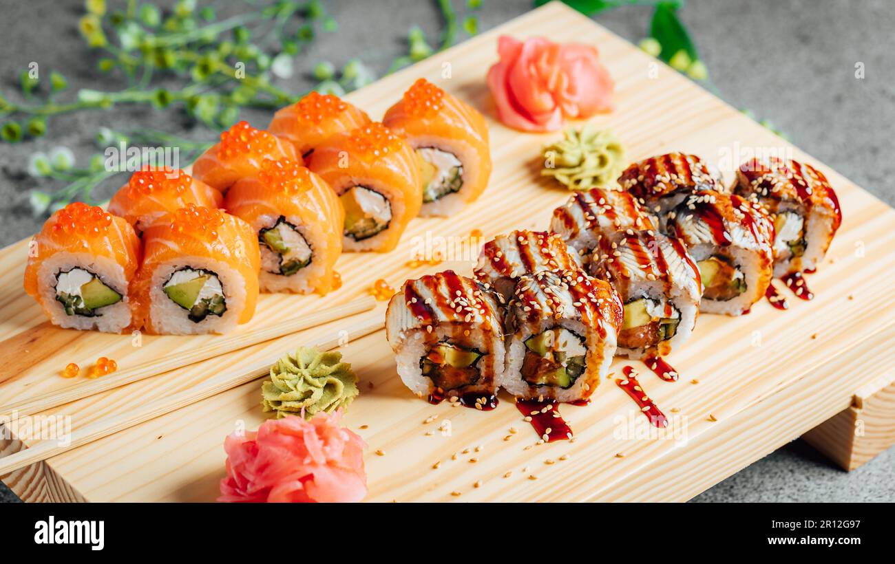 Une variété de petits pains à sushi disposés soigneusement sur une planche à découper en bois, accentuée par une fleur unique au centre Banque D'Images