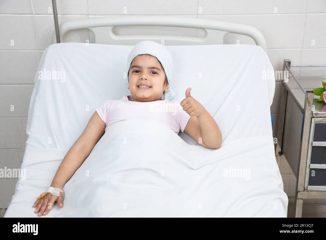 Petite fille souriante enfant patient allongé au lit d'hôpital faire des pouces vers le haut en cours de chimiothérapie. Concept de soins de santé. Banque D'Images