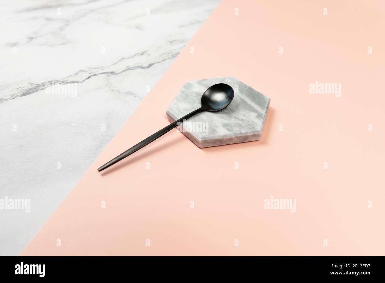 Cuillère à dessert noire sur fond de marbre. Marbre blanc et fond rose. Couverts noirs, espace de copie. Banque D'Images