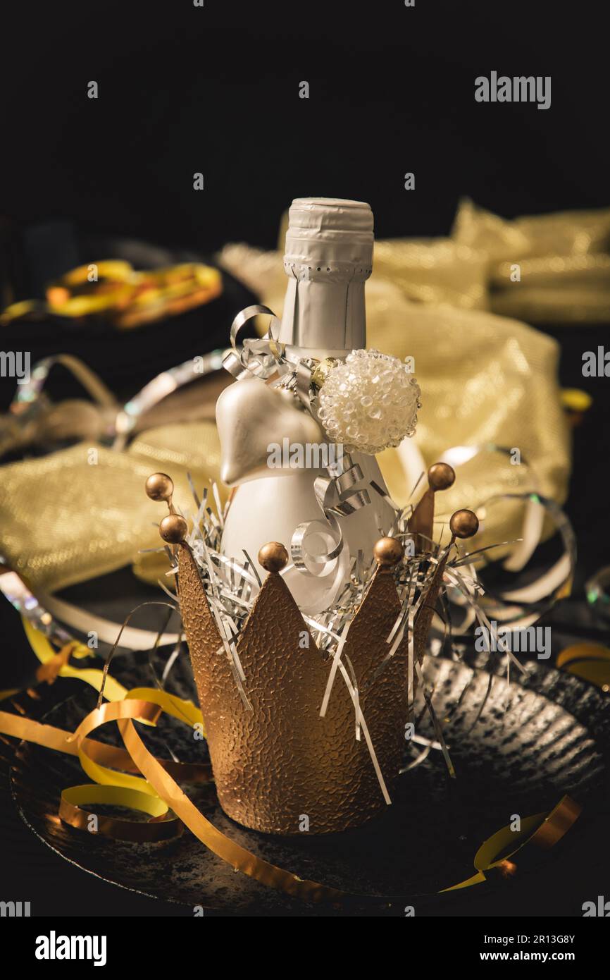 Petite bouteille blanche avec vin mousseux dans une couronne décorative en métal doré, décorée d'un coeur blanc. Verticale. Banque D'Images
