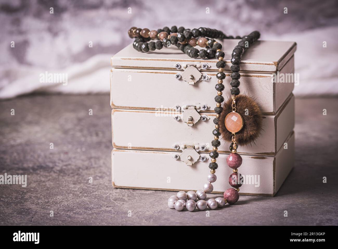 Collier avec perles, bijoux fantaisie, sur une boîte à bijoux en bois blanc, couleurs gris, blanc et rose, fond gris, style vintage Banque D'Images