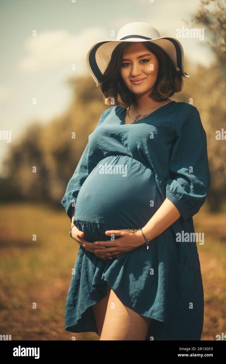 Une femme enceinte avec une robe bleue chapeau blanc dans un champ d'olivier à faible profondeur de champ. Banque D'Images