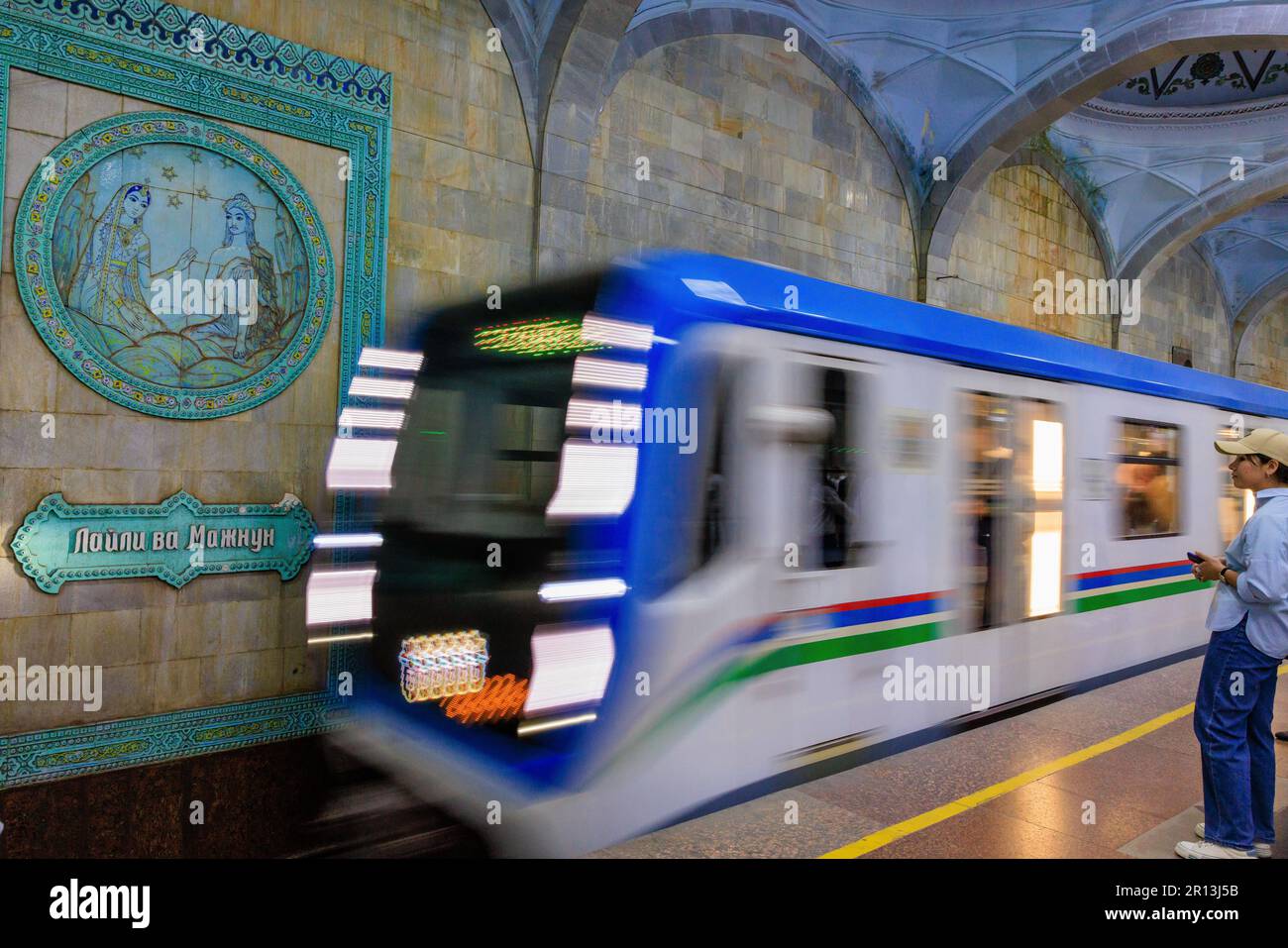 photo à l'obturateur lent du train en mouvement arrivant à la station de métro alisher navoi à tachkent, devant l'un des panneaux représentant l'une de ses histoires Banque D'Images