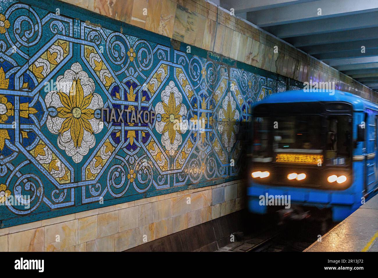 photo à obturation lente d'un train légèrement flou arrivant à la station de métro pakhtakor aux motifs vifs célébrant l'industrie de la cueillette du coton Banque D'Images