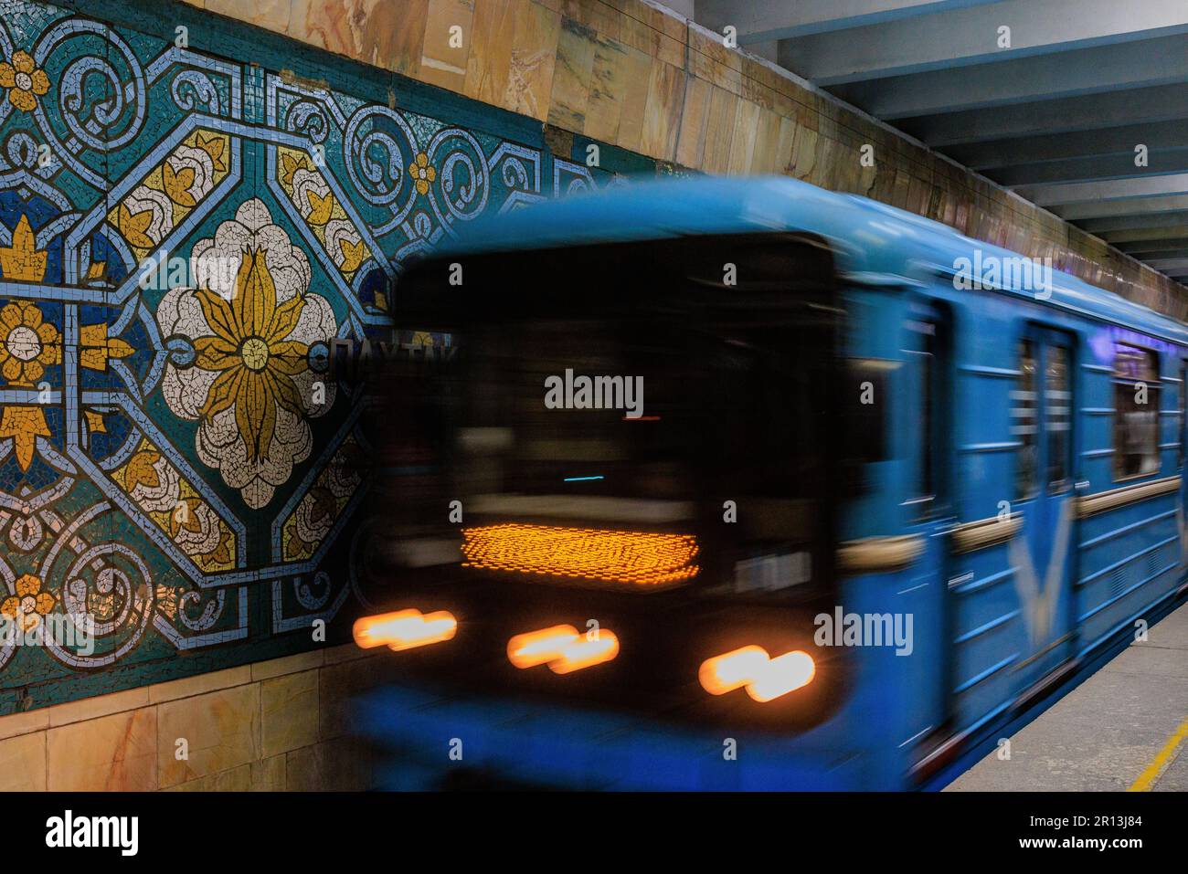 photo à obturation lente d'un train légèrement flou arrivant à la station de métro pakhtakor aux motifs vifs célébrant l'industrie de la cueillette du coton Banque D'Images