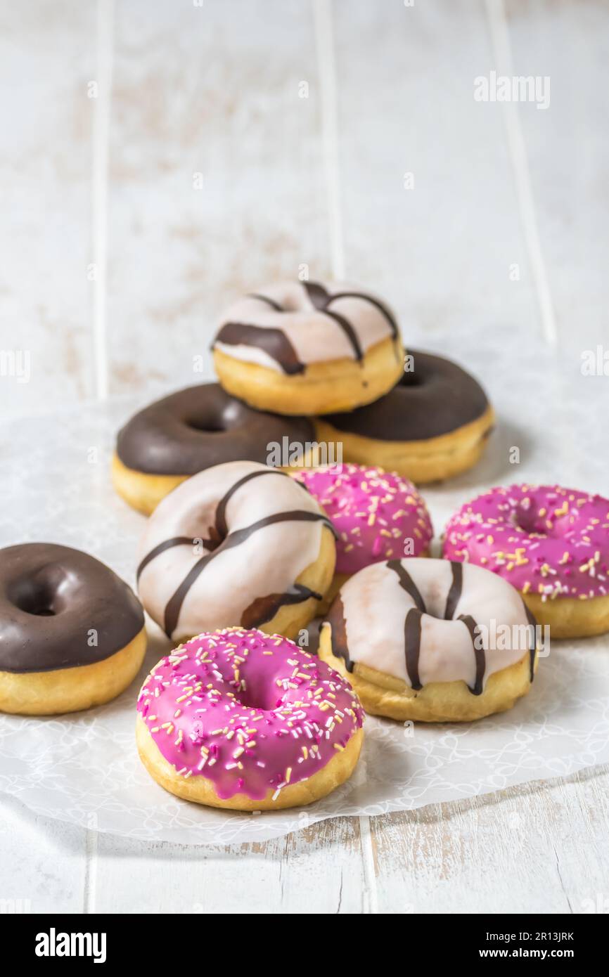 Donuts colorés, Berliner, Krapfen avec glaçage au sucre et chocolat sur fond blanc en bois, vertical avec espace de copie Banque D'Images