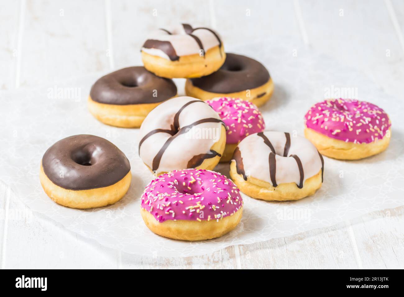 Donuts colorés, Berliner, Krapfen avec glaçage au sucre et chocolat sur fond blanc en bois, vertical avec espace de copie Banque D'Images